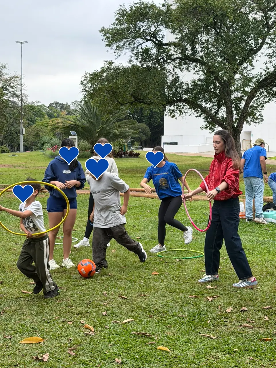 Crianças e voluntárias brincando com bambolês e bola na grama