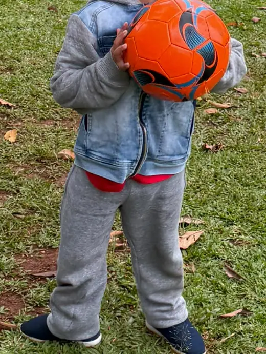 Criança pequena segurando uma bola de futebol laranja
