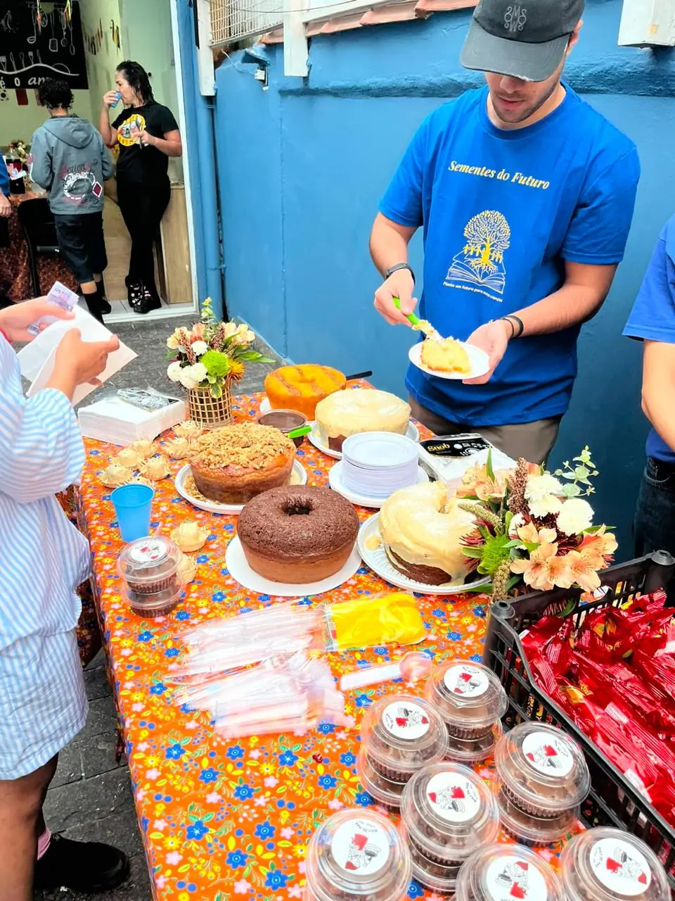 Voluntário servindo bolo numa mesa com toalha florida