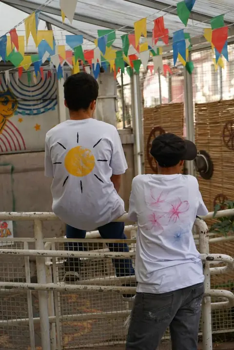 Dois meninos de costas vestindo camisetas brancas pintadas com um sol e flores