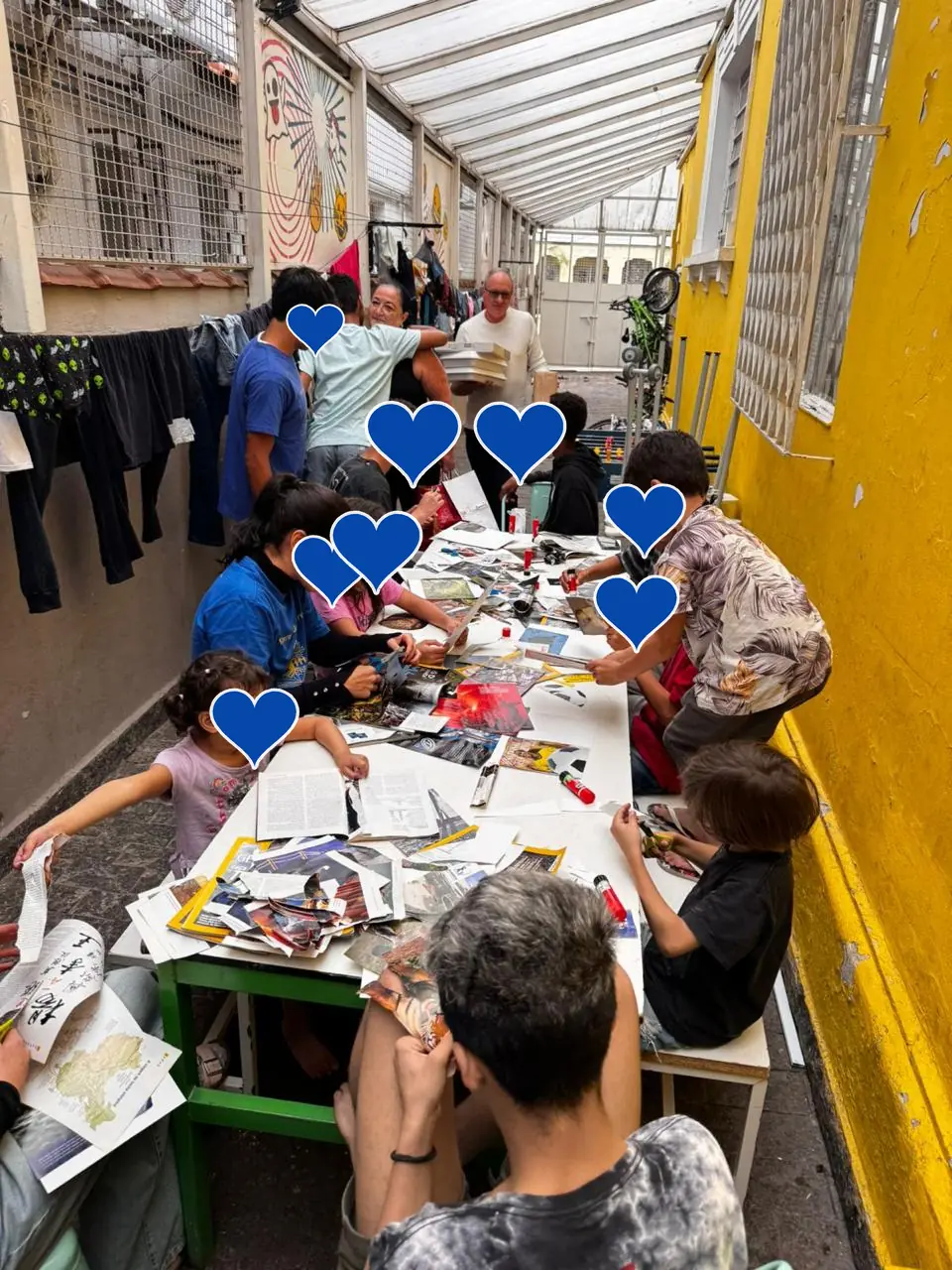 Crianças recortando revistas numa mesa comprida para fazer colagens