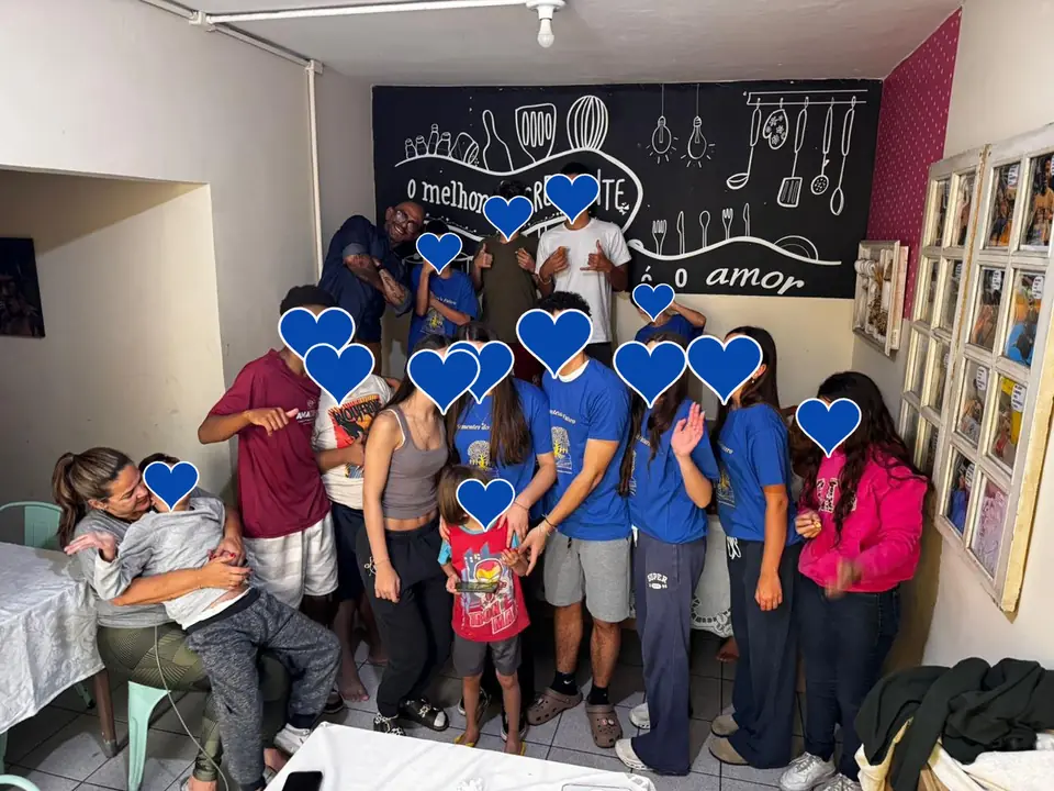 Voluntários e crianças reunidos numa cozinha, diante de um quadro escrito: o melhor ingrediente é o amor