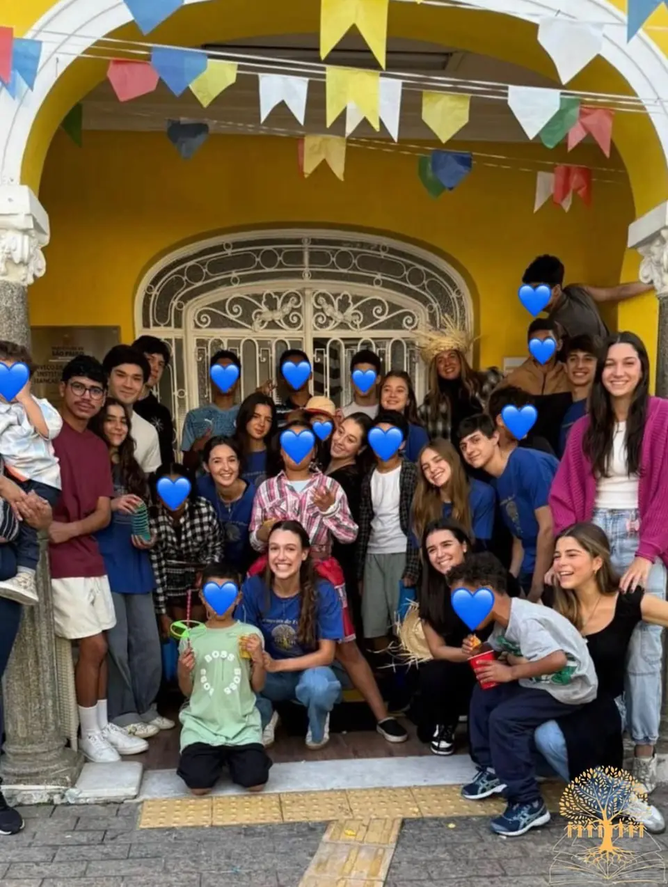 Voluntários e crianças na porta amarela do abrigo, decorada com bandeirinhas de festa junina