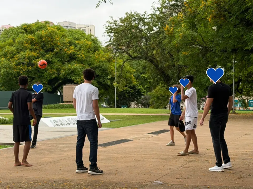 Jovens jogando bola em roda numa praça arborizada