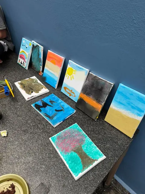 Telas pintadas pelas crianças encostadas numa parede azul